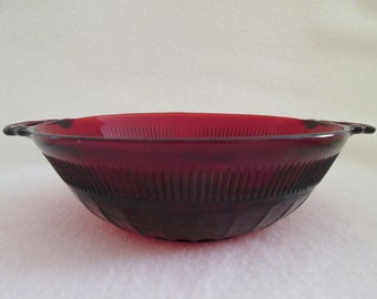 May include: A red glass bowl with two handles. The bowl has a ribbed design and is made of ruby red glass.