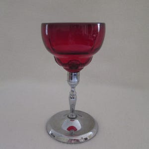 May include: A red glass goblet with a silver base. The goblet has a fluted design and a round base.