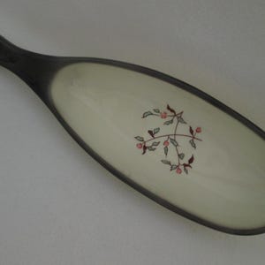 May include: A white ceramic serving dish with a black rim and a floral design. The dish is oval shaped with a long handle.