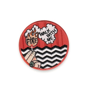Peut inclure: Écusson brodé circulaire rouge. Il présente les mots "FIRE" et "WALK WITH ME", une main tenant une allumette, une flamme, des zigzags noirs et blancs et une bordure rouge. Un accessoire unique.