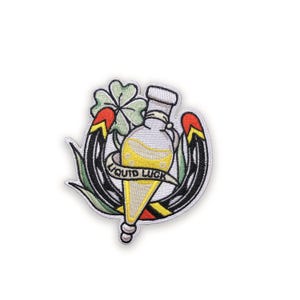 Può includere: Toppa ricamata con un design stilizzato con una bottiglia contenente liquido giallo, un quadrifoglio e un ferro di cavallo. Il testo "LIQUID LUCK" è su uno striscione. La toppa ha accenti neri, verdi, rossi e gialli.