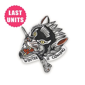 May include: Embroidered patch featuring a snarling wolf head with a dagger. The wolf is black and white with yellow eyes and red accents. Text on the patch reads "WINTER IS COMING". A pink circle with "LAST UNITS" is in the upper left.