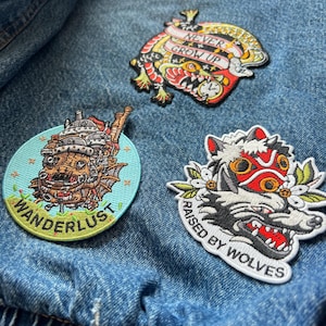 Puede incluir: Tres parches bordados sobre una chaqueta vaquera. Un parche presenta un drag&oacute;n colorido con el texto "NEVER GROW UP". Otro parche tiene un dise&ntilde;o de lobo con el texto "RAISED BY WOLVES". El tercer parche tiene un castillo de dibujos animados con el texto "WANDERLUST".