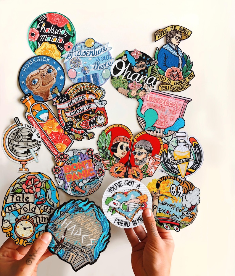 Puede incluir: Una colecci&oacute;n de parches bordados coloridos con varios dise&ntilde;os y texto. Los parches presentan frases como "Hakuna Matata" y "Ohana". Otros parches representan ilustraciones de un dinosaurio, un globo terr&aacute;queo y una pareja.