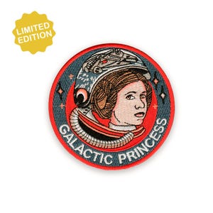 May include: A round, embroidered patch featuring a woman in a space helmet with the text "GALACTIC PRINCESS". The patch has a red border and a blue background with star details. A yellow "LIMITED EDITION" sticker is in the upper left corner.