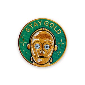 Op de afbeelding: Ronde geborduurde patch met een gouden C-3PO robotkop op een groene achtergrond. De patch heeft de tekst "STAY GOLD" in goud. Geschikt om op kleding of tassen te naaien.