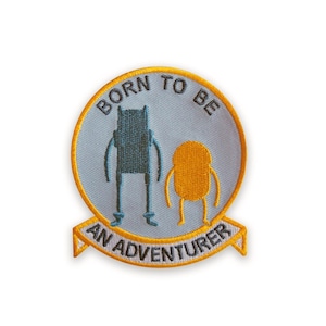 May include: Embroidered patch featuring two cartoon characters inside a light blue circle with the words "BORN TO BE" above and "AN ADVENTURER" below. The patch has a yellow border.