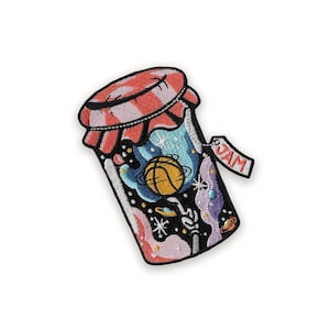 Peut inclure: Écusson brodé représentant un bocal avec un ballon de basket à l'intérieur d'une scène cosmique. Le bocal a un couvercle à carreaux rouges et blancs et une étiquette indiquant "JAM". L'écusson est coloré avec des accents bleus, violets et jaunes.