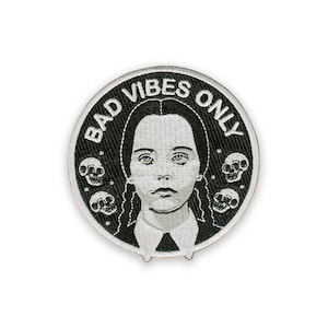 Può includere: Toppa ricamata rotonda in bianco e nero. Il design presenta una ragazza con trecce, teschi e la scritta "BAD VIBES ONLY".