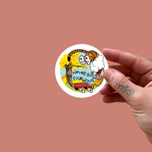 May include: A round sticker featuring a cartoon tiger with orange and black stripes, holding a cloud of cotton candy. The sticker has the text "Never stop EXPLORING" and a tree with autumn leaves. The sticker is on a red wagon.