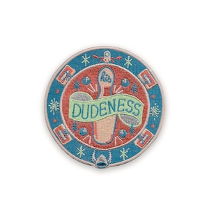 May include: Embroidered patch with a circular design. The patch features a bowling pin with the word "DUDENESS" on a banner. The background is red with blue and white accents, including stars and geometric shapes. The patch has a blue border.