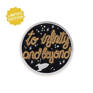 Può includere: Toppa rotonda nera con la scritta dorata "to infinity and beyond". Presenta un razzo bianco e stelle. Un distintivo giallo "edizione limitata" è nell'angolo in alto a sinistra.