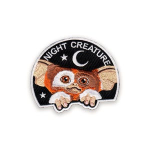 May include: Embroidered patch with a cartoon creature design. The creature has large eyes, brown and white fur, and pointed ears. The patch reads "NIGHT CREATURE" above the creature, with a crescent moon and stars on a black background.