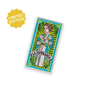 Puede incluir: Parche rectangular con una ilustración estilizada de una mujer con un atuendo azul y blanco, con el texto "LA ESPERANZA" debajo. Una pegatina amarilla de "EDICIÓN LIMITADA" está en la esquina superior izquierda. Borde turquesa.