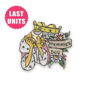 Può includere: Toppa ricamata con un personaggio dei cartoni animati con corona d'oro e veste rosa, con la scritta "mommy's boy" su uno striscione. Elementi floreali circondano la figura e un cerchio rosa indica "LAST UNITS".