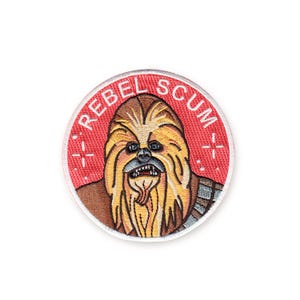 May include: Embroidered patch featuring a Chewbacca design with the text "REBEL SCUM" in a red circle. The patch has a detailed illustration of Chewbacca's face with brown, tan, and black colors. The patch is round and has a white border.