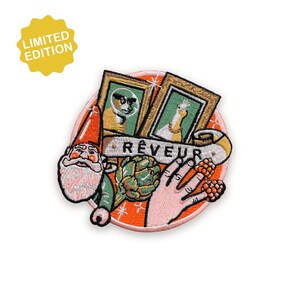 May include: Embroidered patch with a whimsical design featuring a gnome, framed portraits, a hand, and an artichoke on an orange background. The word "Rêveur" is displayed on a banner. A yellow "Limited Edition" tag is in the upper left.