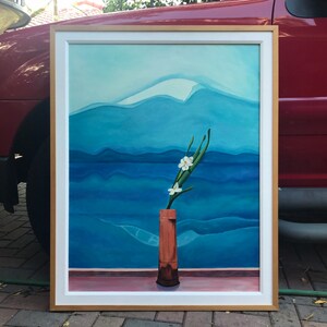 May include: A framed painting of a white flower in a brown vase against a blue and white mountain landscape.