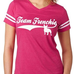 以下が含まれることがあります： ピンクと白の女性のTシャツに、フランスのブルドッグの白いグラフィックと「Team Frenchie」のテキストが描かれています。