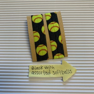 K&ouml;nnte beinhalten: Zwei schwarze elastische Haargummis mit einem Muster aus gelben und roten Softb&auml;llen. Die Haargummis befinden sich auf einer braunen Karte mit einem gelben Haftnotiz, auf dem "Schwarz mit sortierten Softb&auml;llen" steht.