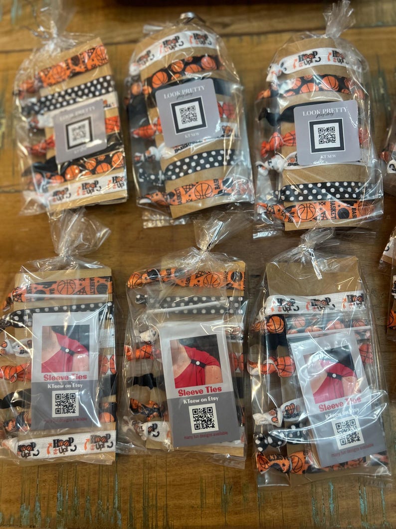 May include: Several packages of hair ties and sleeve ties are displayed. The hair ties feature basketball and polka dot patterns. The sleeve ties are packaged with a tag that reads "Sleeve Ties KTeow on Etsy". The packages are sealed in clear plastic.