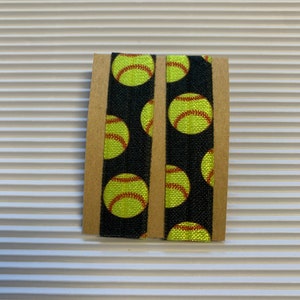 K&ouml;nnte beinhalten: Zwei schwarze Gummib&auml;nder f&uuml;r Haare mit einem sich wiederholenden Muster aus gelben Softball-Designs.