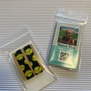 K&ouml;nnte beinhalten: Zwei schwarze und gelbe Softball-elastische Haarb&auml;nder in einer durchsichtigen Plastikt&uuml;te. Die T&uuml;te befindet sich auf einer wei&szlig;en gestreiften Oberfl&auml;che. Eine separate durchsichtige Plastikt&uuml;te enth&auml;lt eine Karte mit dem Text "Sleeve Ties" und "Klisew on Etsy" sowie einen QR-Code. Die Karte sagt auch "many fun designs available".