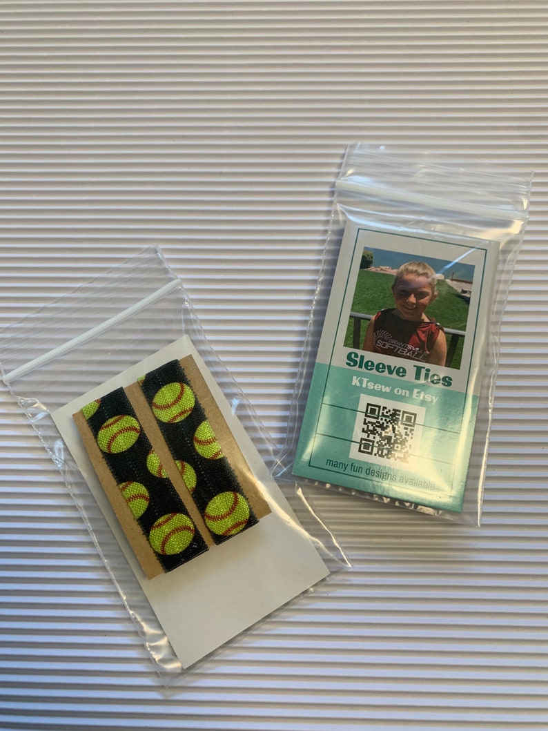 K&ouml;nnte beinhalten: Zwei schwarze und gelbe Softball-elastische Haarb&auml;nder in einer durchsichtigen Plastikt&uuml;te. Die T&uuml;te befindet sich auf einer wei&szlig;en gestreiften Oberfl&auml;che. Eine separate durchsichtige Plastikt&uuml;te enth&auml;lt eine Karte mit dem Text "Sleeve Ties" und "Klisew on Etsy" sowie einen QR-Code. Die Karte sagt auch "many fun designs available".