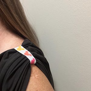 May include: Black top with a white strap featuring a repeating pattern of yellow, orange, and pink Mickey Mouse heads. The strap is sewn onto the shoulder of the top.