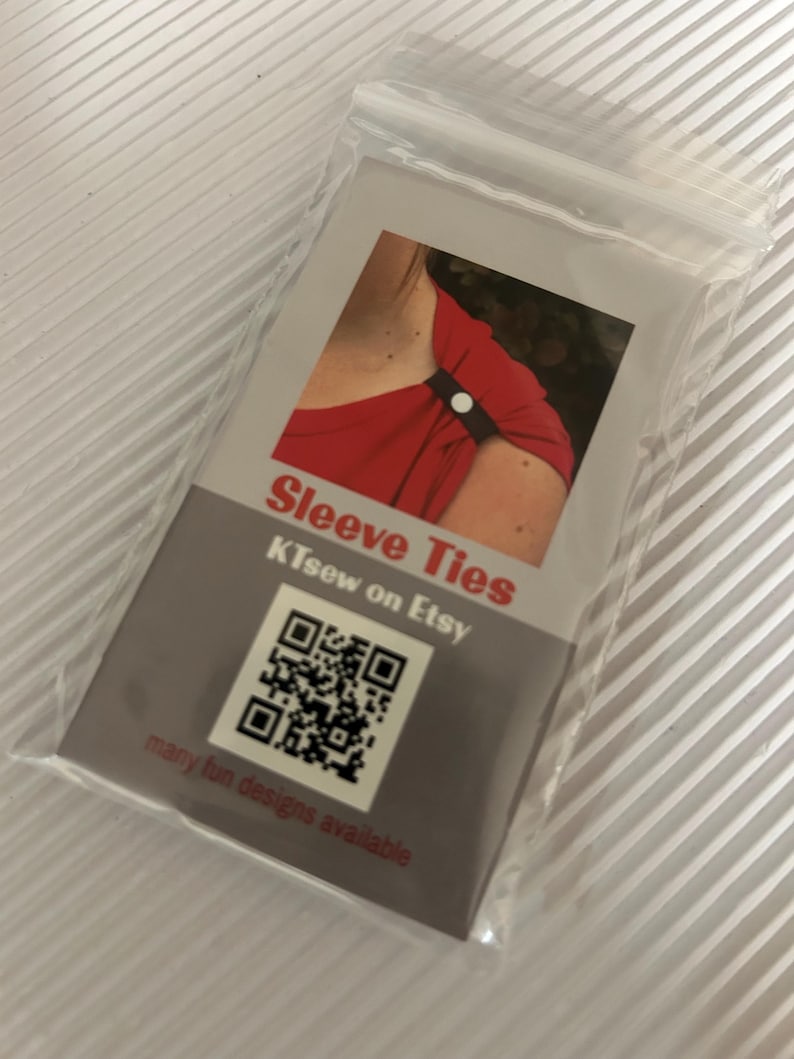 May include: A clear plastic bag containing a product card for "Sleeve Ties." The card features a photo of a black sleeve tie on a red top. Text includes "KTsew on Etsy" and a QR code, with the phrase "many fun designs available."