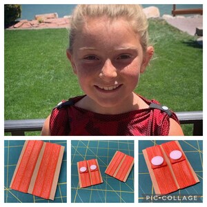 May include: Two sets of orange elastic hair ties with white buttons on a brown card. The hair ties are on a green cutting mat.