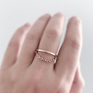 May include: A gold ring with a thin band and a delicate chain attached. The chain is looped through the band, creating a unique and modern design.