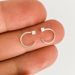 May include: A pair of small silver hoop earrings with square accents.