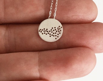 May include: A silver necklace with a circular pendant featuring a dotted pattern. The pendant is about 1 inch in diameter.