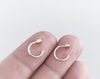 May include: A pair of small silver hoop earrings with a gold accent on each hoop.