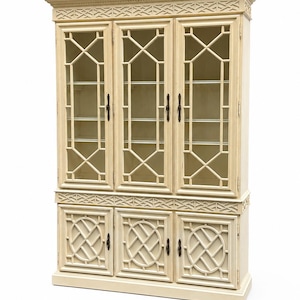 May include: A tall, off-white wooden cabinet featuring three upper glass-paneled doors with a geometric lattice design and three lower solid doors with circular fretwork patterns. The piece includes decorative carved molding along the top and middle.