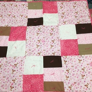 May include: A pink and brown patchwork quilt with a pattern of small pink hearts and white dogs. The quilt is made of various fabrics and is sewn together with pink thread.