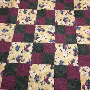 May include: A quilt with a checkered pattern featuring alternating squares of burgundy and dark green fabric. Each square is decorated with a floral print of vines, leaves, and grapes in shades of blue, pink, and white on a beige background.