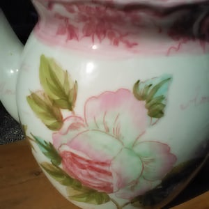 May include: White porcelain teapot with a pink and green floral design. The teapot has a lid and a handle.