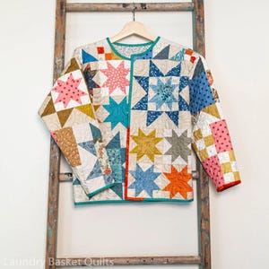 May include: A colorful patchwork quilt jacket with a teal trim and a star pattern. The jacket is made of various fabrics in shades of pink, blue, yellow, orange, and green.