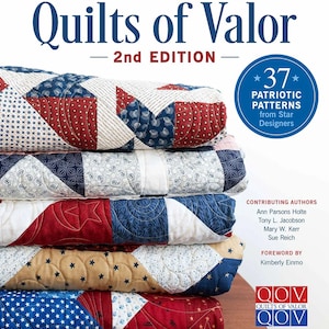 May include: A stack of patriotic quilts with red, white, and blue patterns. The book "Quilts of Valor" is visible, with text indicating 37 patriotic patterns from Star Designers. The quilts are folded and stacked on a wooden surface.