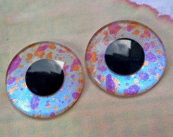 Puede incluir: Dos ojos saltones grandes, redondos, iridiscentes azul, rosa y dorado con pupilas negras.