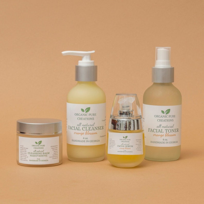 May include: Four bottles of organic skincare products with orange blossom scent. The products include a facial cleanser, facial toner, facial serum, and cleansing balm. All products are labeled "Organic Pure Creations" and are handmade in Georgia.