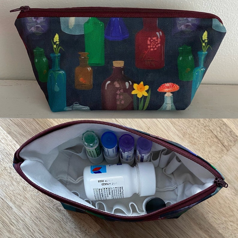 May include: A cosmetic bag with a dark blue background featuring colorful bottles and flowers. The bag has a burgundy zipper and interior. The inside of the bag is white and contains several small bottles and a white pill bottle.