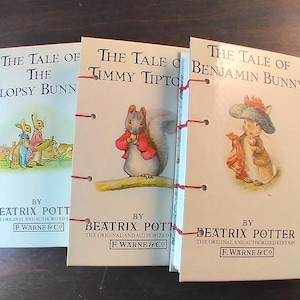 May include: Three small, bound books with colorful illustrations on the covers. The books are titled "The Tale of the Flopsy Bunnies", "The Tale of Timmy Tiptoes", and "The Tale of Benjamin Bunny". Each book is by Beatrix Potter and published by F. Warne & Co.