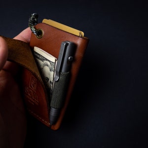 Peut inclure: Un portefeuille en cuir marron avec une sangle, un stylo et un billet de dollar &agrave; l'int&eacute;rieur. Le portefeuille porte un logo "SOMA".