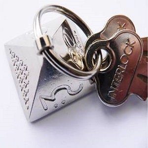 May include: A silver pyramid-shaped keychain with the number "23" engraved on one side. The keychain has a silver ring and is attached to two silver keys with the word "INTERLOCK" engraved on one key.