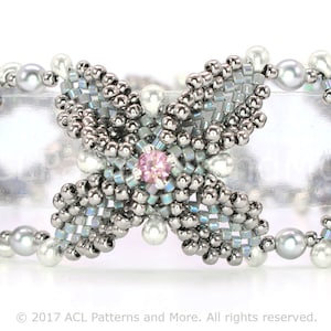 以下が含まれることがあります： 中央に蝶のデザインが施された、シルバーのビーズブレスレット。ブレスレットは主にシルバーで、水色と白のビーズがアクセントになっています。蝶の中央にはピンク色の宝石、片側には青色の宝石があります。真珠のようなビーズで飾られています。