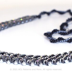 May include: A black and silver beaded necklace with a crystal-like finish. The necklace is made of two strands of beads, one black and one silver, that are woven together in a zig-zag pattern. The necklace is approximately 18 inches long and has a magnetic clasp.