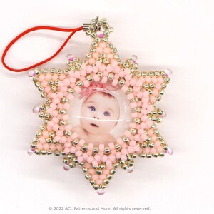 May include: A pink and gold beaded star-shaped ornament with a clear plastic photo insert featuring a baby girl. The ornament has a red string attached for hanging.